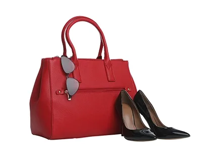 Stylish red handbag with black high-heeled shoes and sunglasses resting on the side, displayed on a white background.
