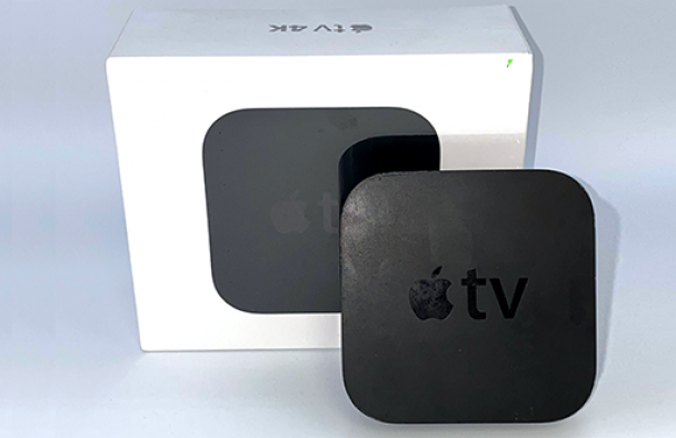 An Apple TV video player and its box sit on a table with a grey background.