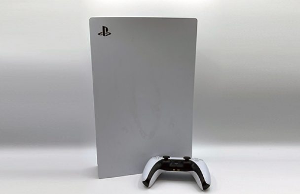 A PlayStation and a controller on display with a grey background.