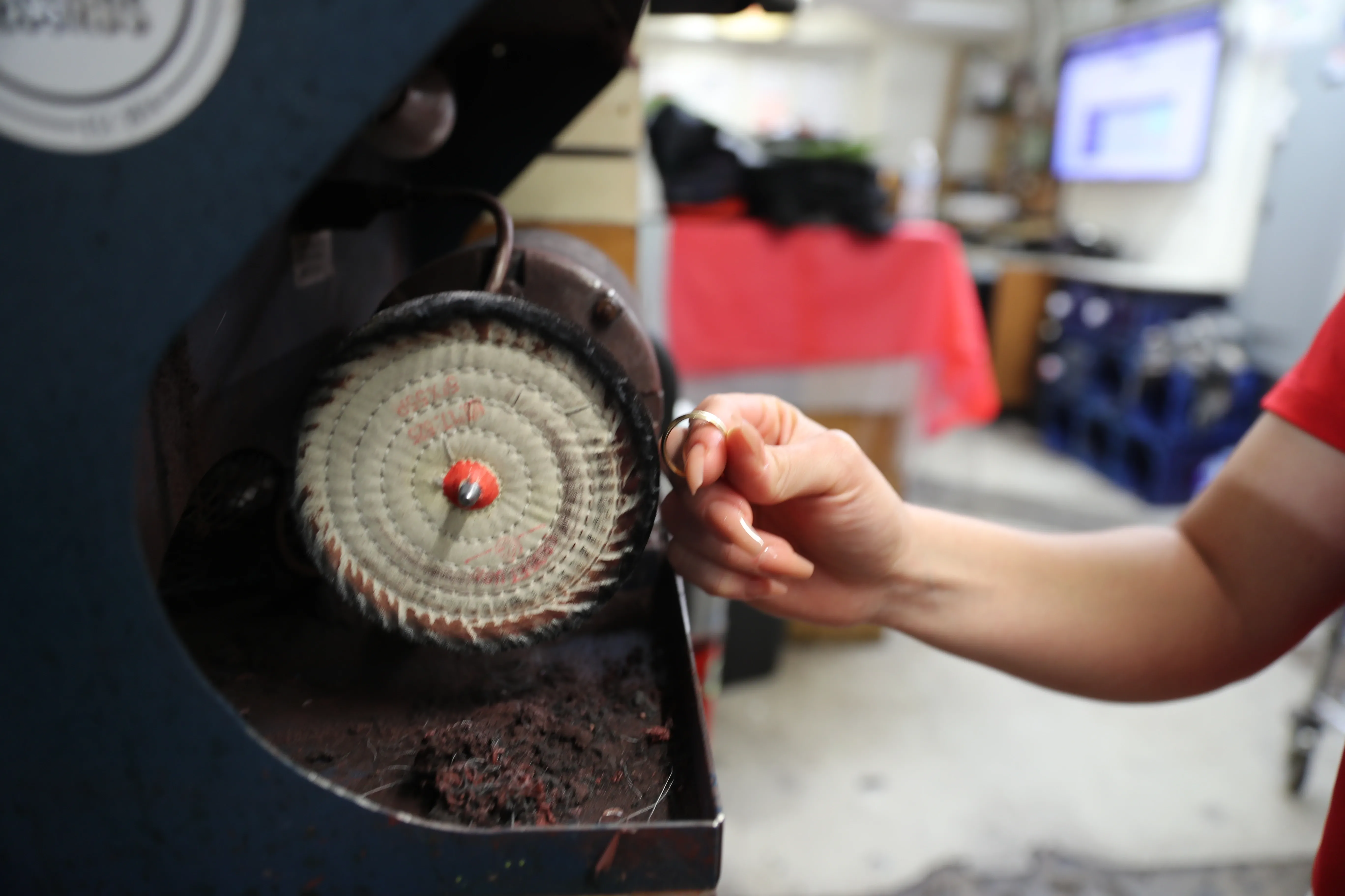 A team member is buffing a ring with a machine in the back room.