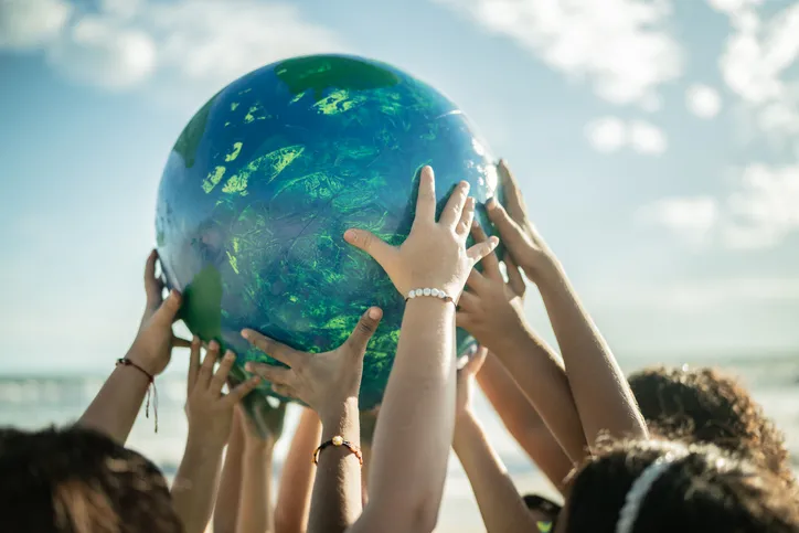 Kids arms holding up a globe on the beach near the ocean.