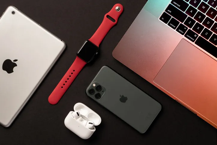 An iPad, Airpods, iPhone, Apple Watch, and Mac book sit on a black table.