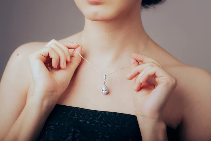 A close up image of women in a black dress with a silver necklace showing it off.