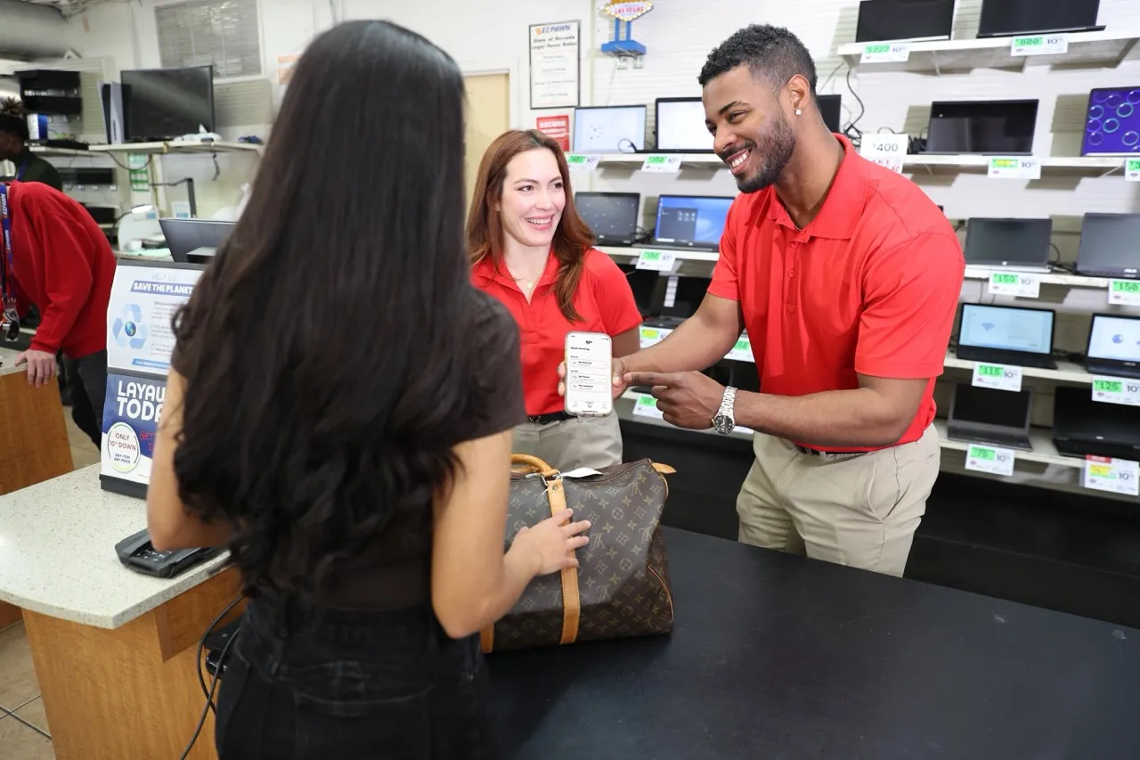 A wide shot of two EZPAWN team members helping a customer with a Louis VuittonTM bag while showing them how to use the EZ+ app.