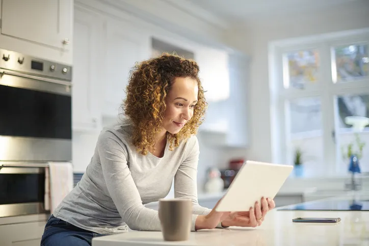A women in her kitchen is viewing her iPad while smiling.
