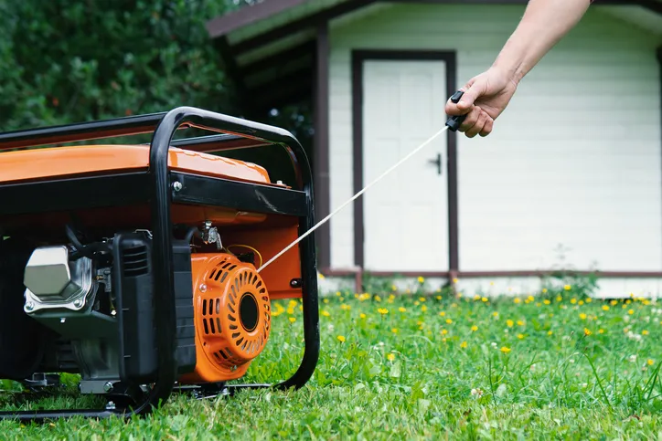 A close up shot of an orange generator. A hand and arm are seen pulling the start cord.