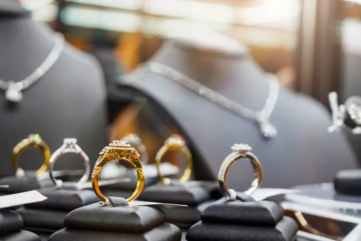 A picture of a jewelry display with engagement rings in the front and necklaces in the background out of focus.