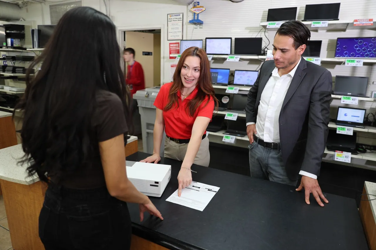 An EZPAWN team member and store manager are assisting a customer with a loan at the counter.