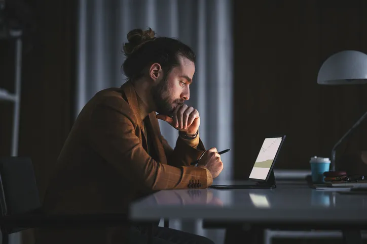 A man sitting at a table with a laptop and pen in hand looking at charts.