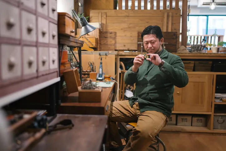 A man in a workshop is inspecting a piece of jewelry.