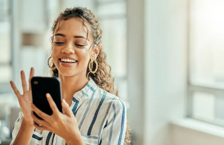 A young girl holding her phone with a big smile with her hand about to press something.