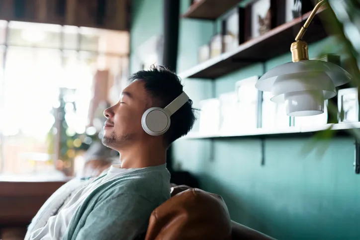 A man sitting on a chair with headphones on while looking very relaxed.